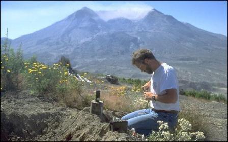 Vulkanoloog die een seismograaf installeert, op de achtergrond de vulkaan Mount St. Helens na de eruptie van 18 mei 1980